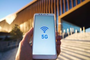 man hand holding a smartphone and 5g signal symbol on screen with broadcast antenna icon on city background. High speed mobile web connection technology concept.